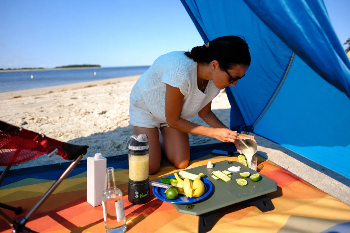 Mujer preparando un batido de plátano y limón con HEWE Blend GO en la playa.